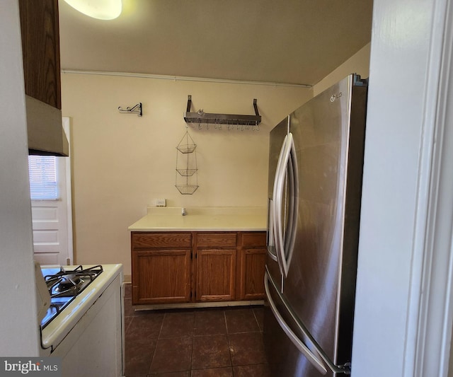 kitchen with stainless steel fridge, dark tile patterned floors, and white range with gas cooktop