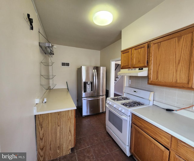 kitchen with dark tile patterned floors, decorative backsplash, white gas range, and stainless steel fridge