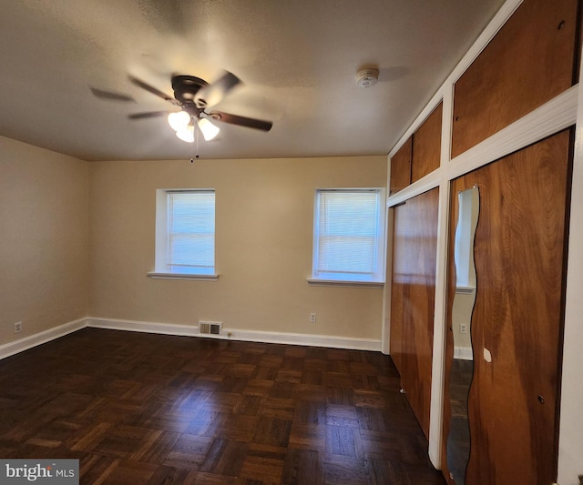 unfurnished bedroom featuring dark parquet flooring, multiple windows, and ceiling fan