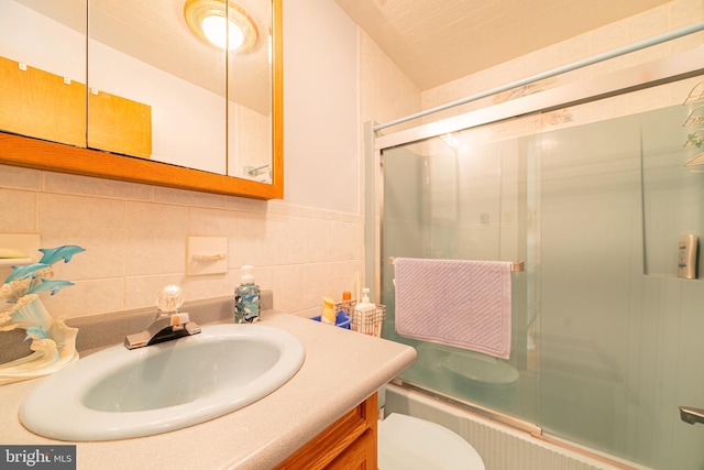 full bathroom featuring tile walls, vanity, bath / shower combo with glass door, toilet, and decorative backsplash