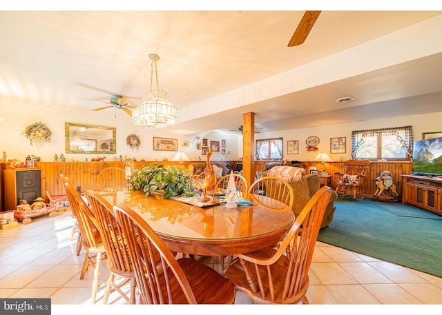 tiled dining room with wood walls and ceiling fan with notable chandelier