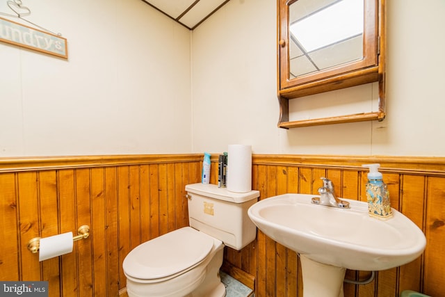 bathroom featuring toilet, wooden walls, sink, and vaulted ceiling