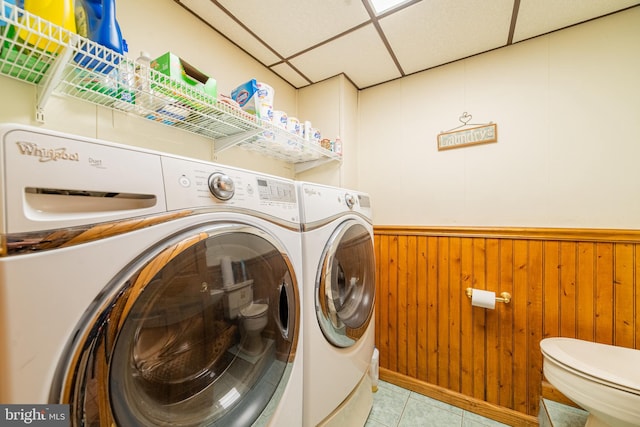 laundry room featuring wood walls, light tile patterned floors, and washer and dryer