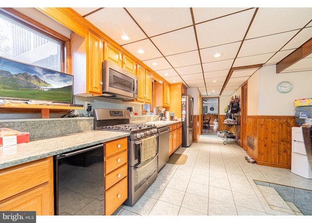 kitchen featuring light stone counters, light tile patterned flooring, stainless steel appliances, wooden walls, and a drop ceiling