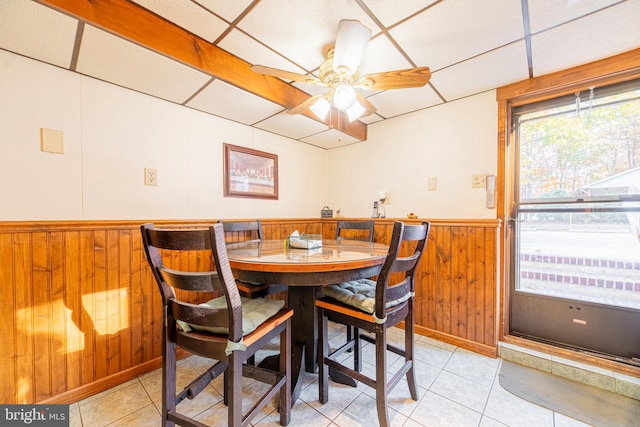 dining area with light tile patterned flooring, a paneled ceiling, wooden walls, and ceiling fan