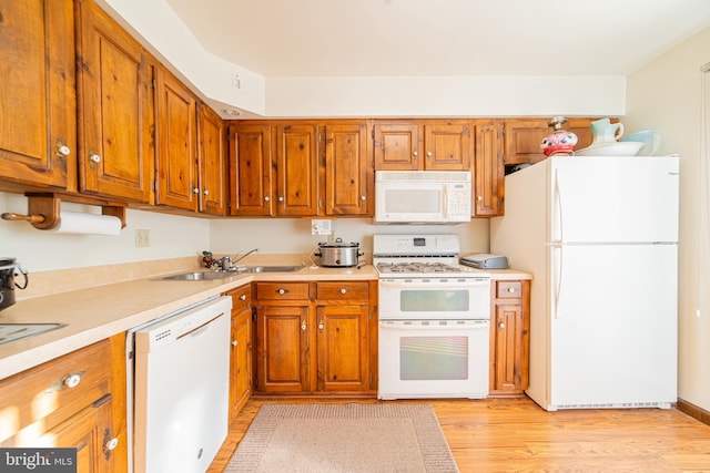 kitchen with light wood-type flooring, white appliances, and sink