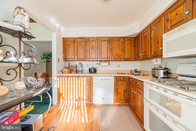 kitchen with light wood-type flooring, white appliances, and sink