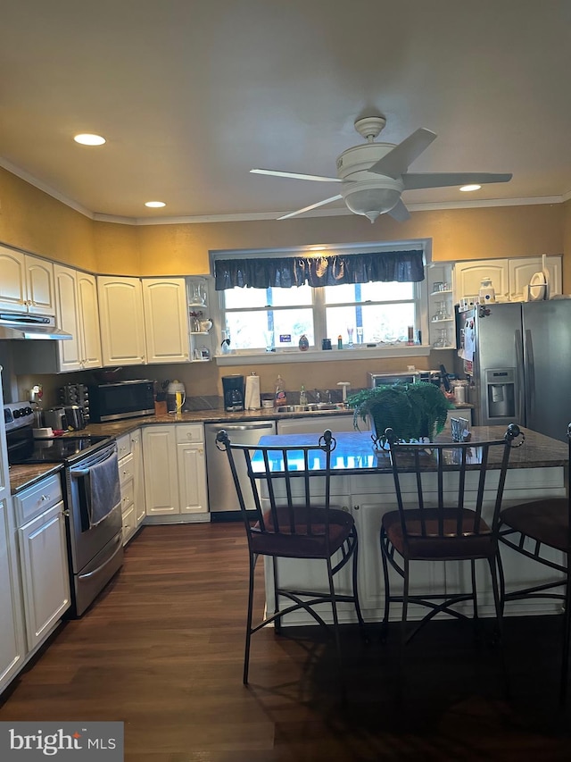 kitchen with crown molding, appliances with stainless steel finishes, dark hardwood / wood-style flooring, white cabinetry, and a breakfast bar area