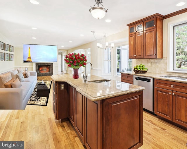 kitchen featuring sink, light hardwood / wood-style flooring, stainless steel dishwasher, pendant lighting, and a kitchen island with sink