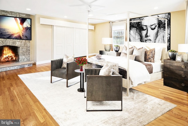 bedroom with ceiling fan, a stone fireplace, and wood-type flooring