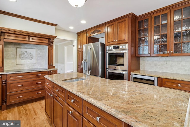 kitchen with sink, wine cooler, light stone countertops, appliances with stainless steel finishes, and light hardwood / wood-style floors