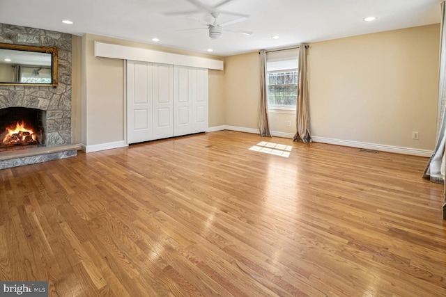 unfurnished living room featuring a stone fireplace, ceiling fan, and light hardwood / wood-style flooring