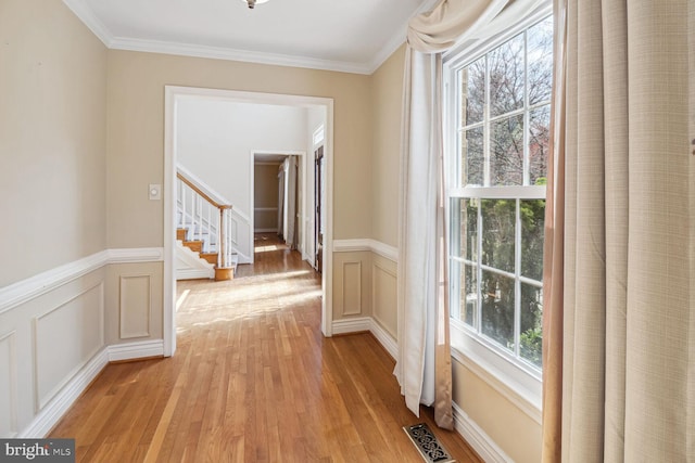 hallway with light wood-type flooring, a wealth of natural light, and ornamental molding