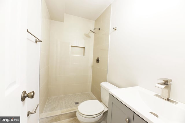 bathroom featuring a tile shower, vanity, and toilet