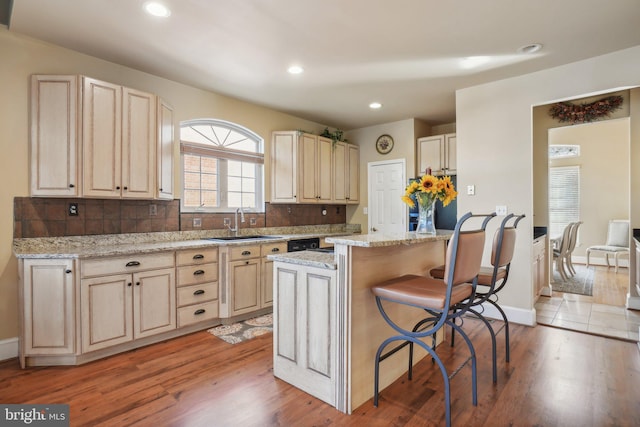 kitchen with light stone countertops, sink, a breakfast bar, light hardwood / wood-style floors, and a center island