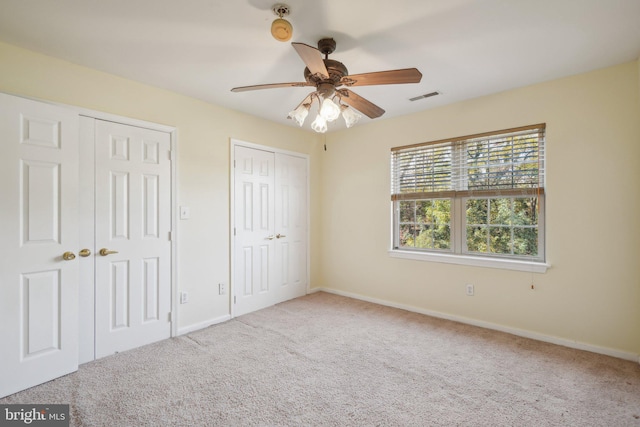 unfurnished bedroom featuring multiple closets, carpet flooring, and ceiling fan