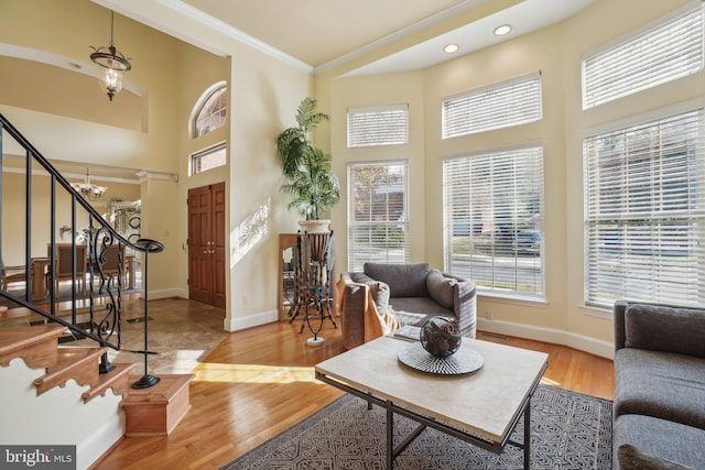 living room featuring light wood-type flooring, a chandelier, ornamental molding, and a towering ceiling