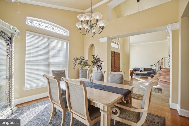 dining space featuring ornamental molding, ornate columns, an inviting chandelier, hardwood / wood-style floors, and a high ceiling