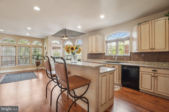 kitchen with a kitchen island, black dishwasher, light stone countertops, decorative backsplash, and a breakfast bar