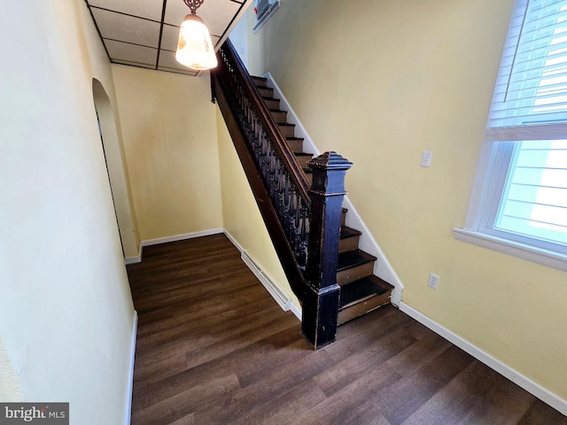 staircase with wood finished floors, baseboards, arched walkways, and a paneled ceiling
