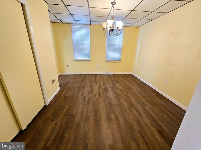 unfurnished dining area with dark hardwood / wood-style floors, a notable chandelier, and a drop ceiling