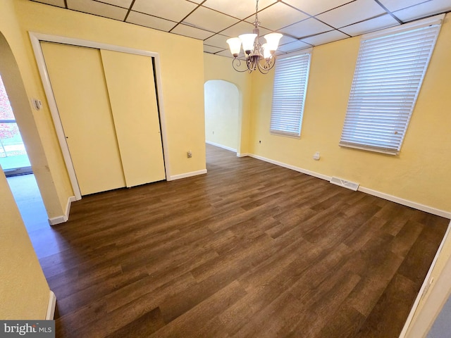 unfurnished dining area featuring a paneled ceiling, dark wood-type flooring, and a chandelier