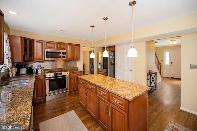 kitchen with light stone counters, dark hardwood / wood-style flooring, stainless steel appliances, sink, and decorative light fixtures