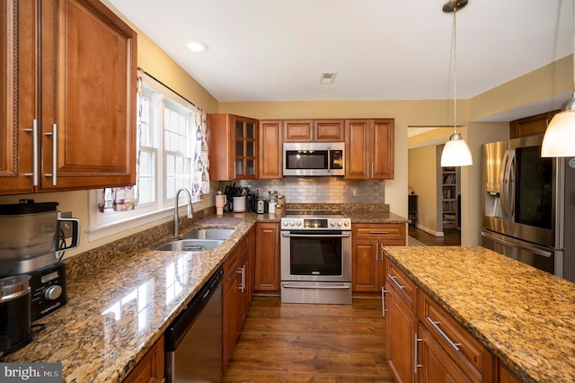 kitchen featuring dark hardwood / wood-style flooring, appliances with stainless steel finishes, light stone countertops, sink, and decorative light fixtures