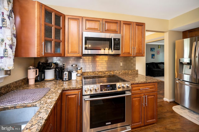 kitchen with appliances with stainless steel finishes, decorative backsplash, light stone counters, and dark hardwood / wood-style flooring