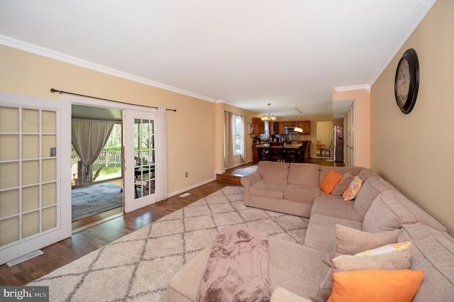 living room with wood-type flooring, ornamental molding, and an inviting chandelier