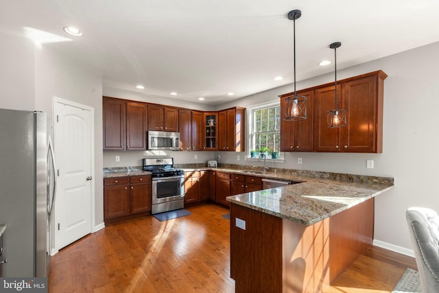 kitchen featuring pendant lighting, a breakfast bar, hardwood / wood-style floors, kitchen peninsula, and stainless steel appliances