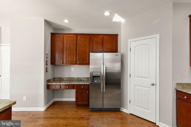 kitchen featuring stainless steel fridge with ice dispenser, light hardwood / wood-style flooring, and light stone counters