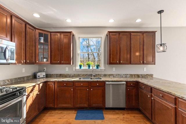 kitchen with light wood-type flooring, light stone counters, stainless steel appliances, sink, and hanging light fixtures