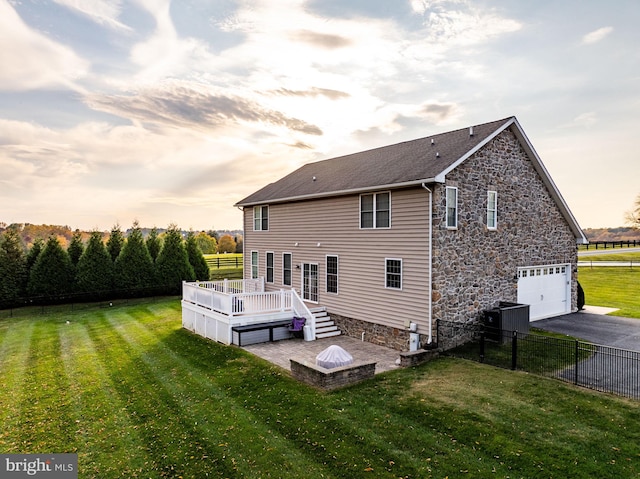 back house at dusk with a yard, a garage, and a wooden deck