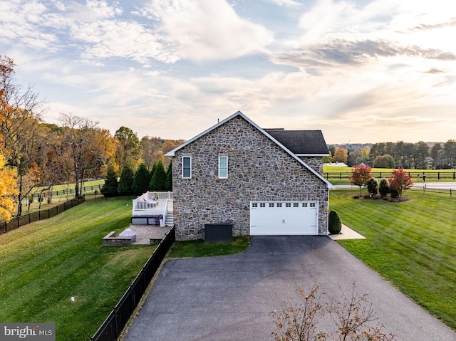 property exterior at dusk with central AC, a yard, a rural view, and a garage