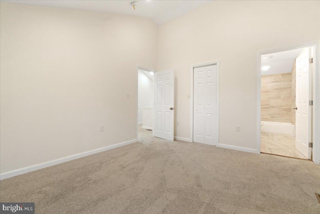 unfurnished bedroom featuring connected bathroom, light carpet, and a high ceiling