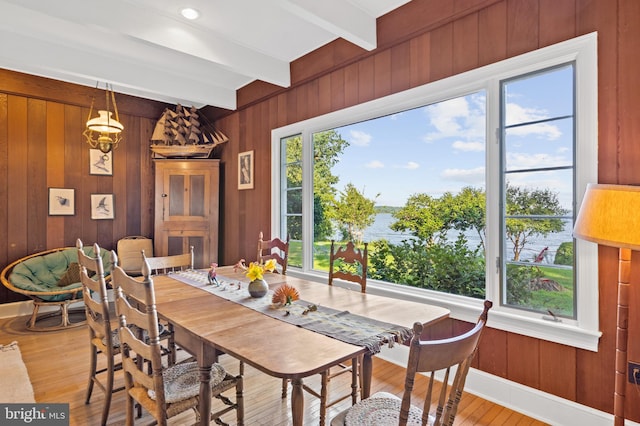 dining area featuring wood walls, beam ceiling, light wood-type flooring, and plenty of natural light