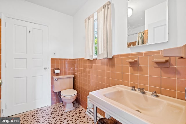 bathroom with tile walls, sink, toilet, and tile patterned flooring