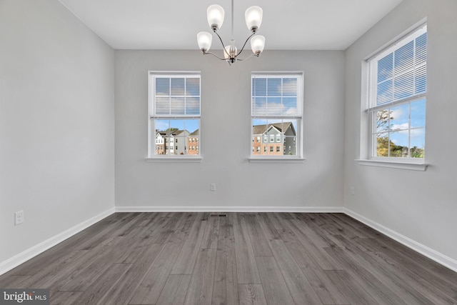 spare room with a chandelier, hardwood / wood-style floors, and a healthy amount of sunlight