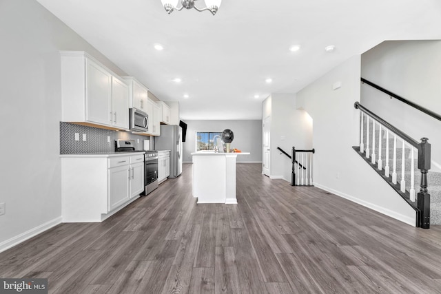 kitchen with white cabinets, backsplash, appliances with stainless steel finishes, dark wood-type flooring, and a center island