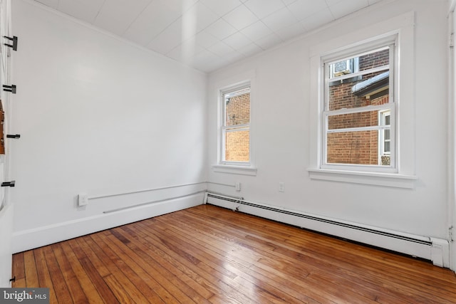 spare room featuring light hardwood / wood-style floors, a baseboard heating unit, a healthy amount of sunlight, and ornamental molding