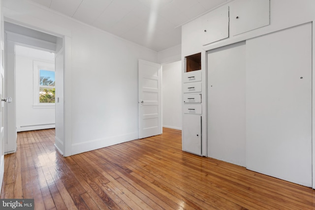 unfurnished bedroom with a closet, wood-type flooring, and baseboard heating