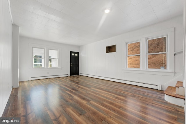 unfurnished living room featuring a baseboard heating unit and dark hardwood / wood-style floors