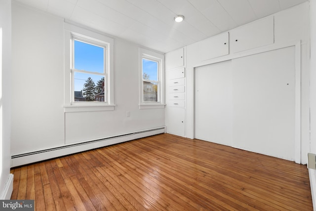 unfurnished bedroom with baseboard heating, hardwood / wood-style flooring, and a closet