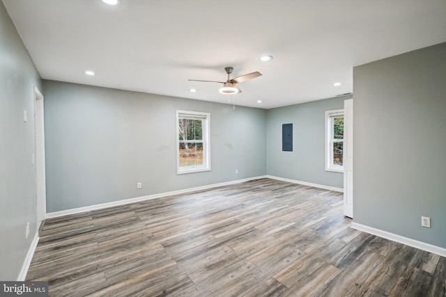 spare room featuring electric panel, a wealth of natural light, wood-type flooring, and ceiling fan