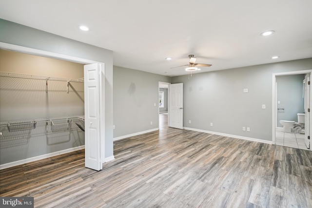 unfurnished bedroom with hardwood / wood-style flooring, ceiling fan, ensuite bath, and a closet