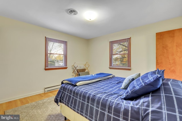 bedroom featuring hardwood / wood-style flooring, baseboard heating, and multiple windows