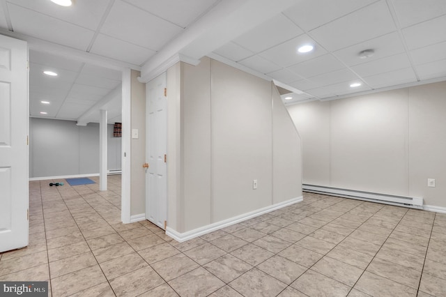 basement with baseboard heating, light tile patterned floors, and a drop ceiling