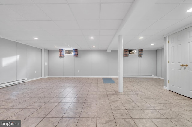 basement featuring a baseboard radiator, a paneled ceiling, and light tile patterned flooring