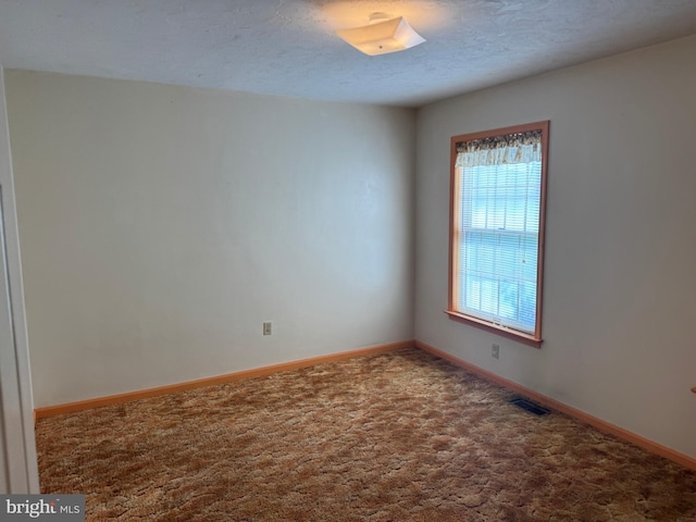 empty room featuring carpet flooring, a textured ceiling, visible vents, and baseboards